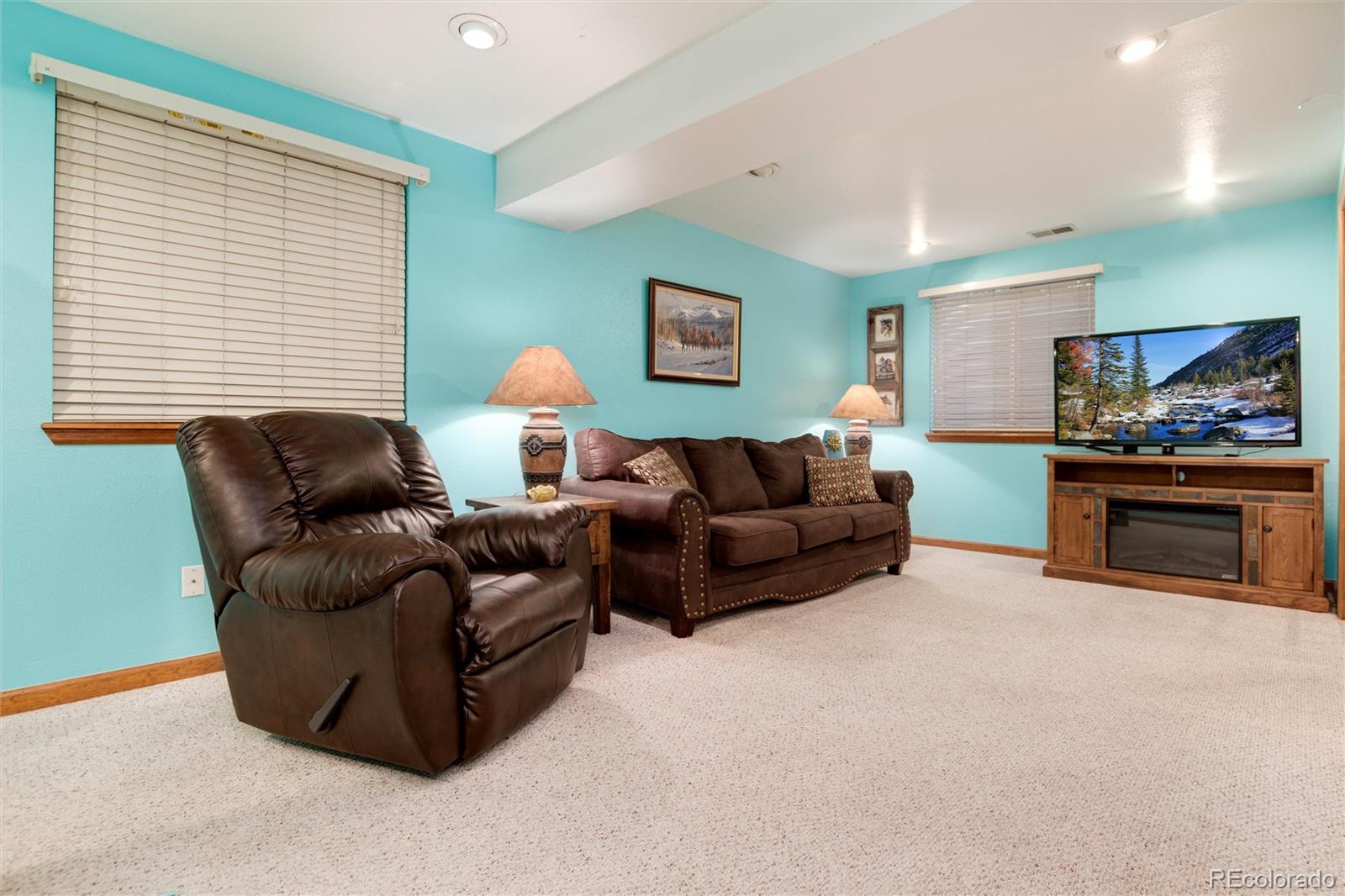 Living room with turquoise walls, brown leather seating, beige carpet, and a television above a fireplace console.