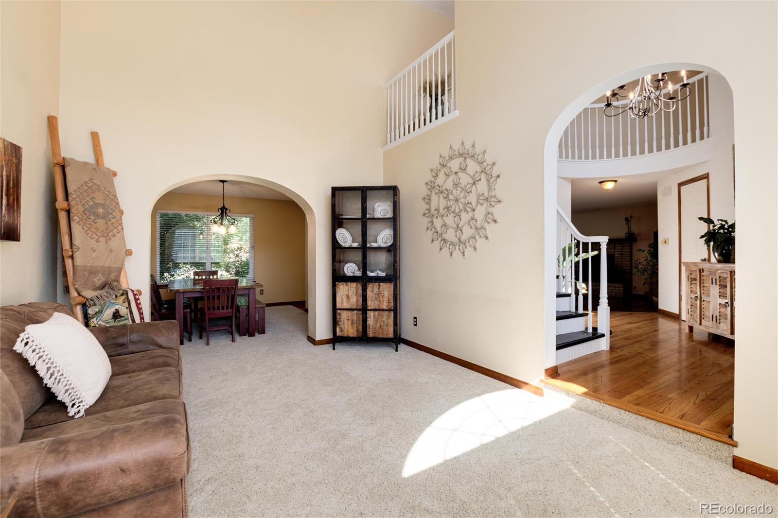 Living room with arched openings to a dining area and a hardwood-floored entry with staircase.