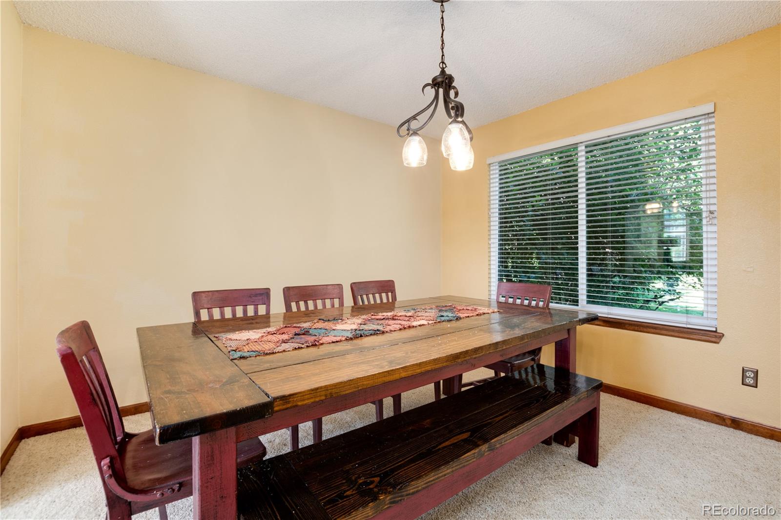 Dining room with a rustic wood table and bench beneath a two-light pendant, beside a wide window.