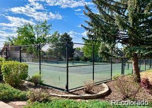Fenced outdoor tennis court bordered by trees and landscaping.