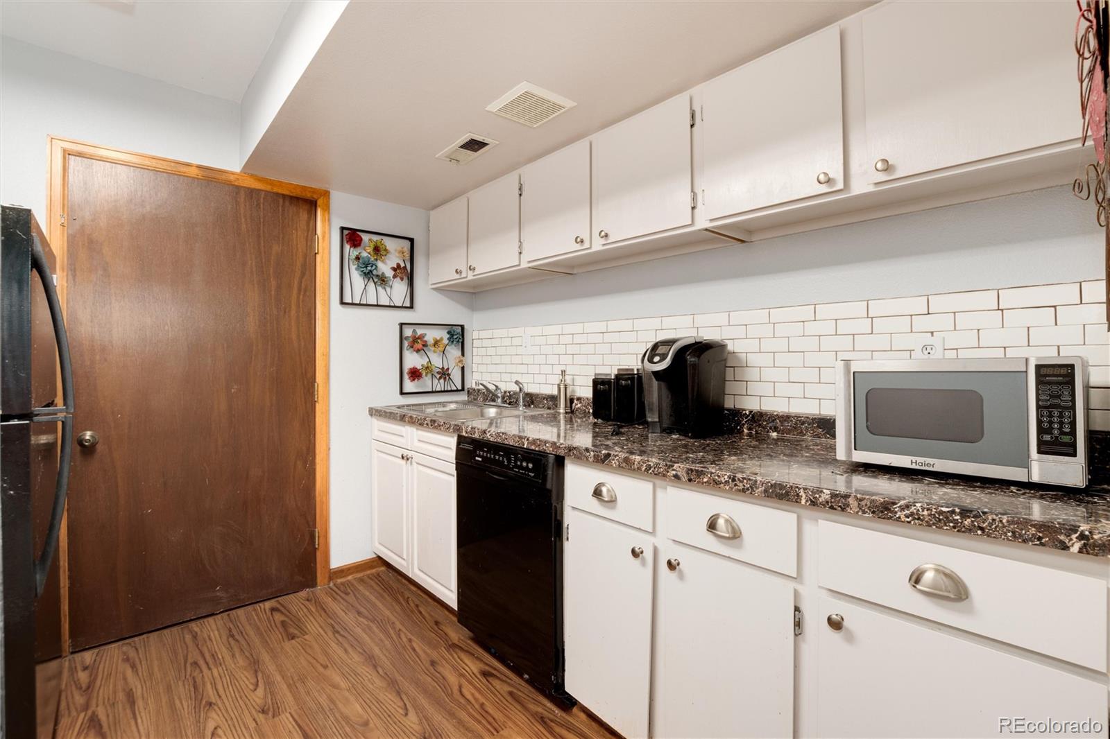 Kitchen with white cabinets, subway tile backsplash, dark counters, and wood-look flooring.