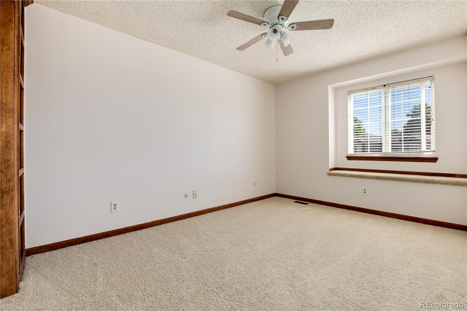 Empty carpeted bedroom with a ceiling fan and a window above a built-in ledge.