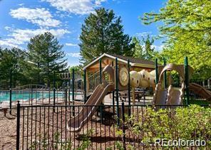 Fenced playground with climbing structure and slides beside a swimming pool.