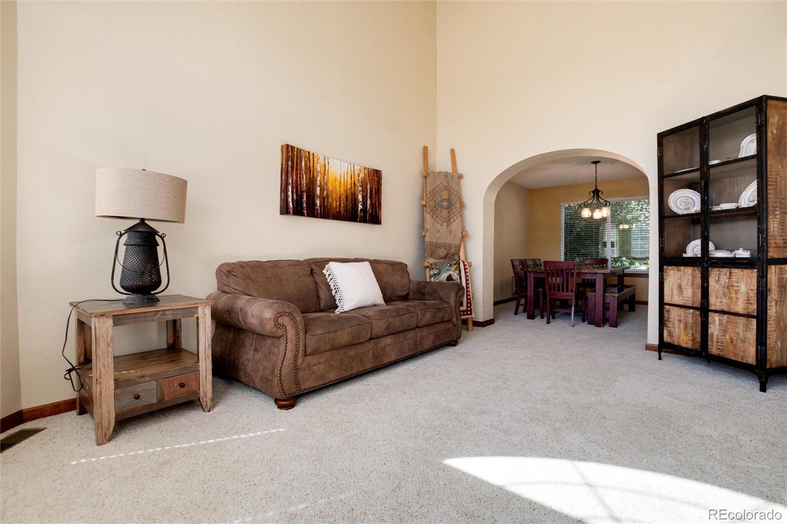 Furnished living room with a brown sofa, carpeted floor, and arched opening to the dining area.