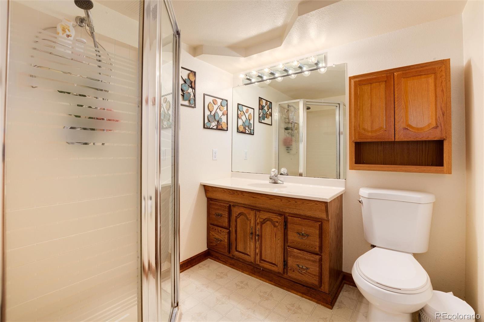Bathroom with glass shower, wood vanity and cabinetry, large mirror, and toilet.
