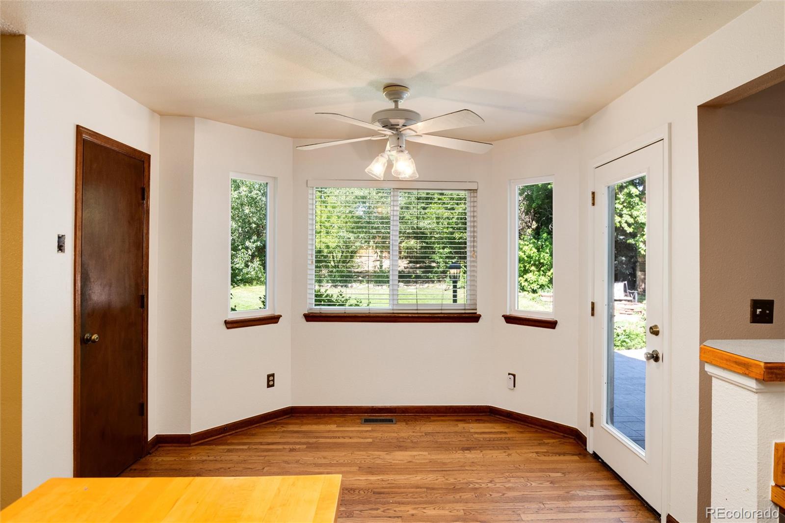 Dining nook with hardwood floors, a ceiling fan, bay windows, and a glass-paneled door to the yard.