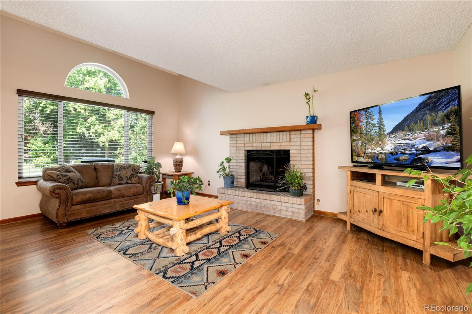 Living room with a brick fireplace, arched window, and wood-look flooring.