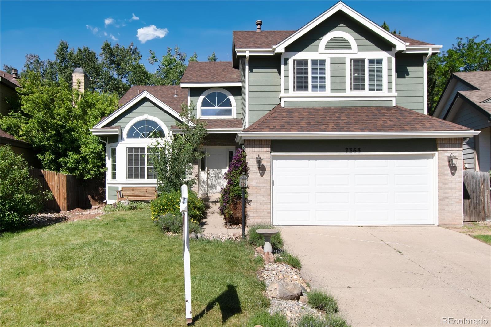 Two-story sage-green house with arched windows, white trim, and a brick-accented double garage.