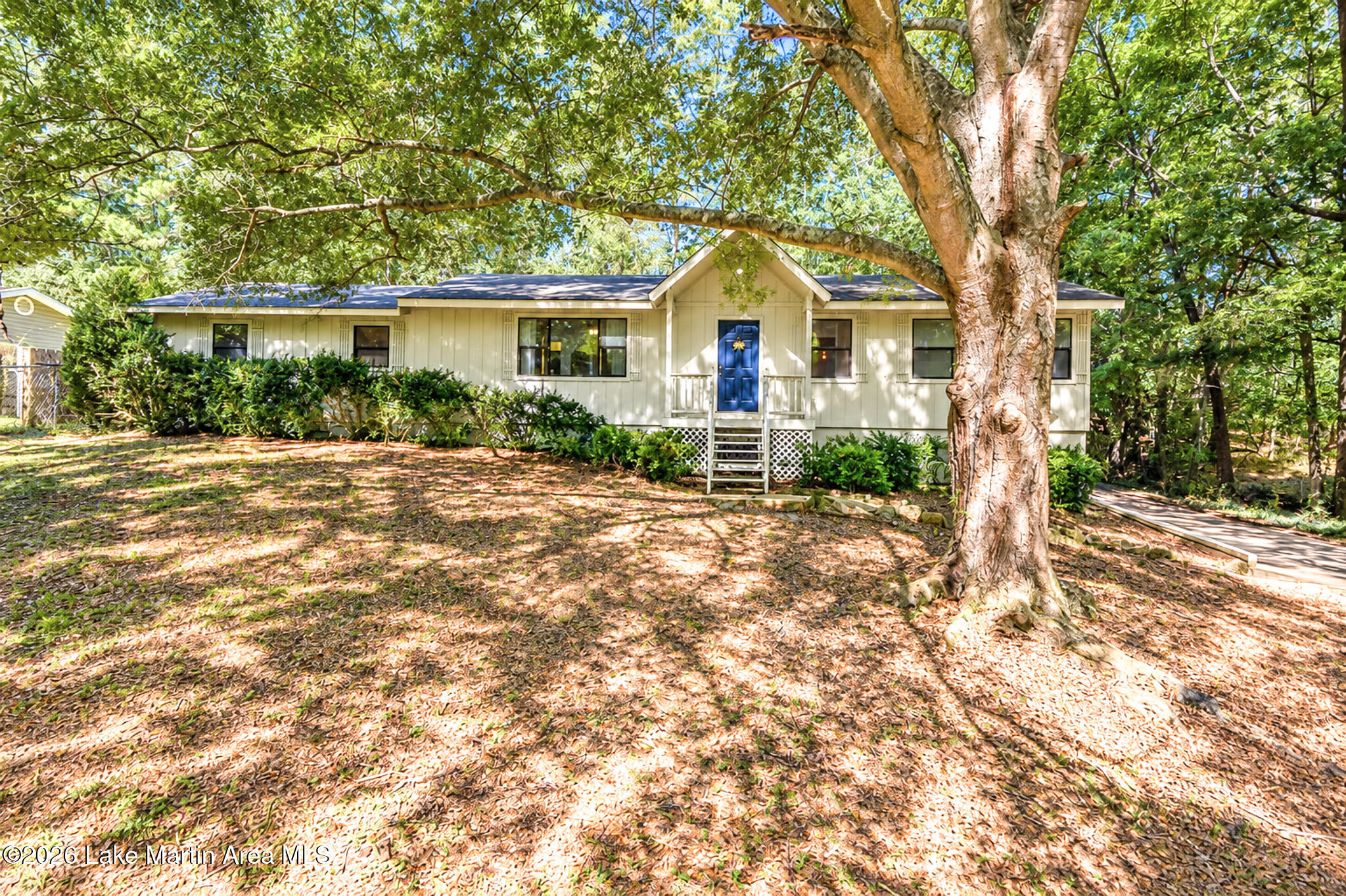 Single-story home with a blue front door beneath a large tree on a leafy lot.