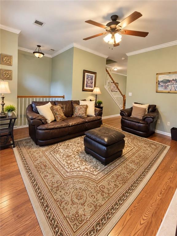 Living room with leather seating, a patterned rug, hardwood floors, and a staircase.