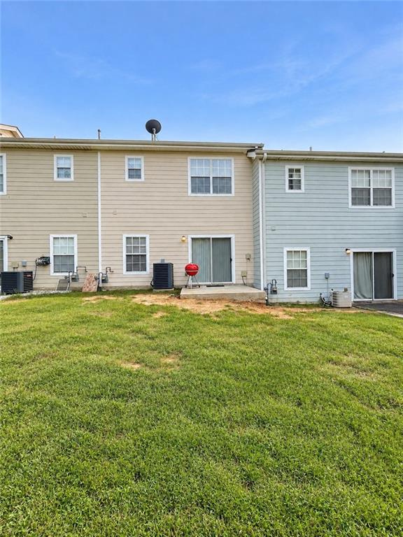 Rear exterior of an attached home with two-tone siding, sliding doors, a red grill, and a grassy yard.
