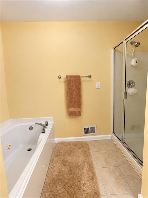 Bathroom with a jetted tub and glass-enclosed shower beside a tan tiled floor.