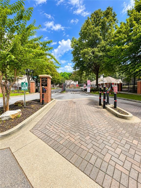 Gated community entrance with a brick-paved driveway, brick columns, and mature trees.