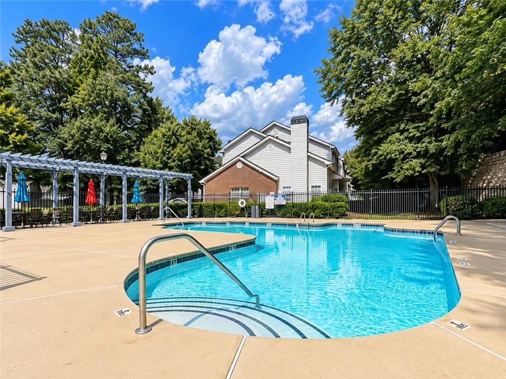 Outdoor swimming pool with curved entry steps, pergola seating, and trees.