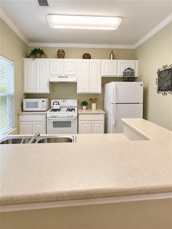 Kitchen with white cabinets and appliances, a window-side sink, and a broad peninsula countertop.