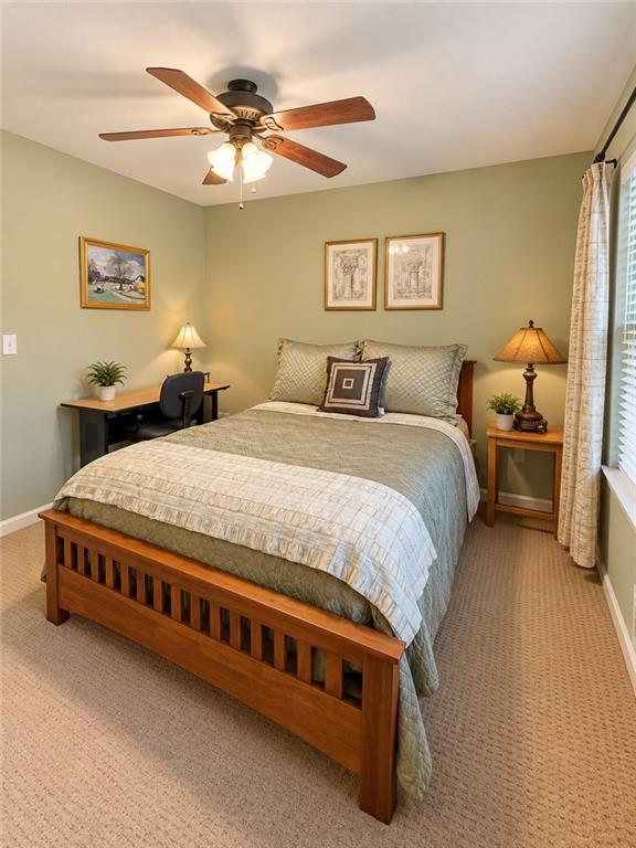 Bedroom with a wooden bed, small desk, ceiling fan, and curtained window.