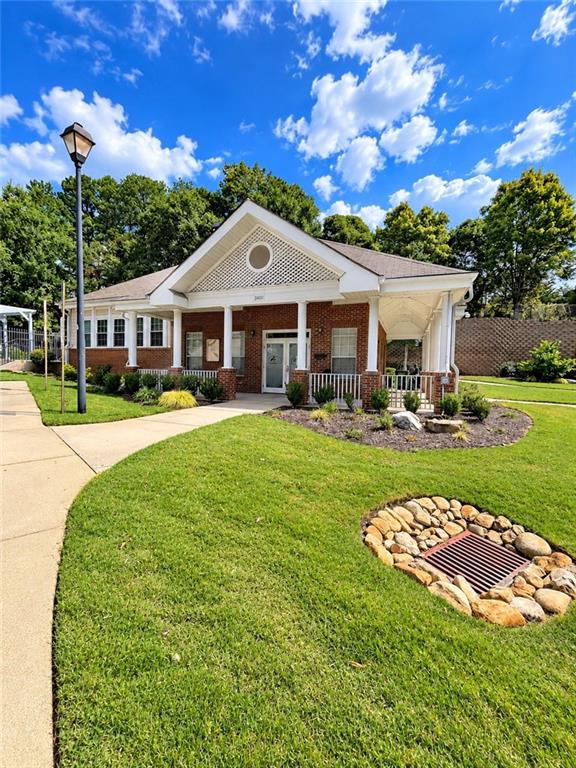 Brick building with a white gabled entrance, covered porch, and landscaped lawn.