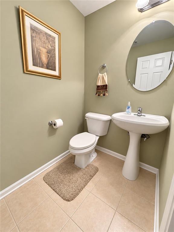 Bathroom with sage-green walls, a pedestal sink, round mirror, and framed artwork.