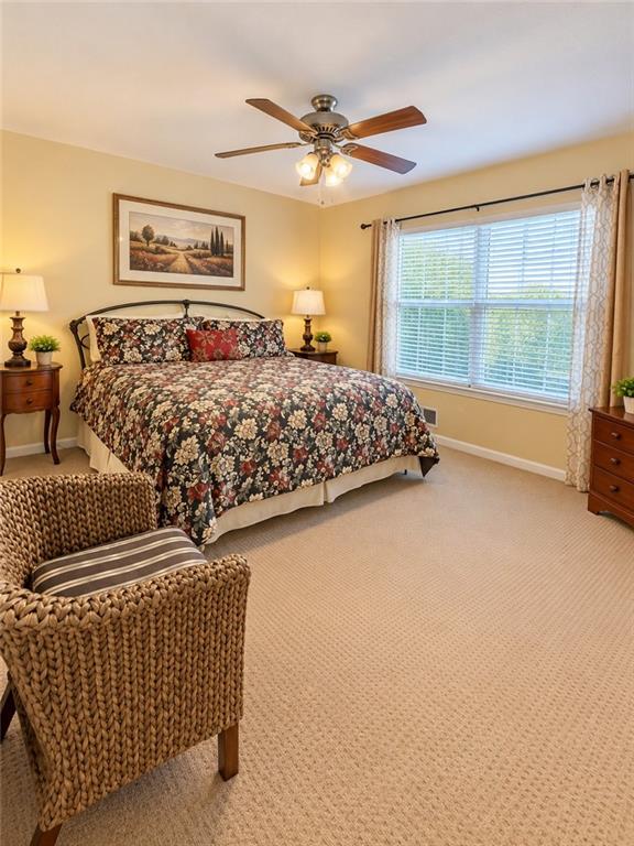 Bedroom with a floral bedspread, large window with blinds, and woven armchair.