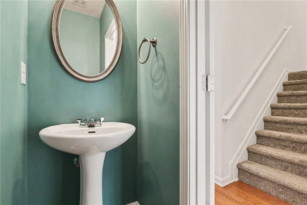 Bathroom with teal walls and pedestal sink beside a carpeted staircase.