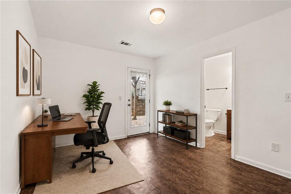 Home office with a wooden desk and chair, glass-paneled exterior door, and adjoining bathroom.