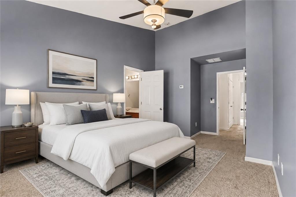 Staged bedroom with a white bed, upholstered bench, gray walls, and ceiling fan.