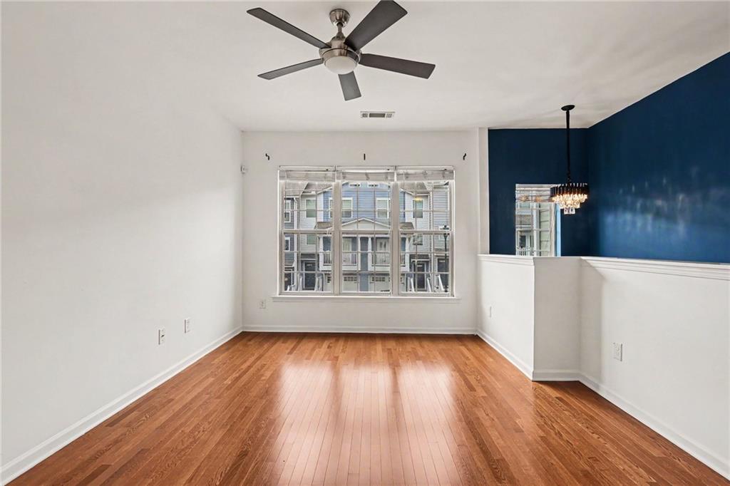 Empty room with hardwood floors, large windows, a ceiling fan, and a navy accent wall.