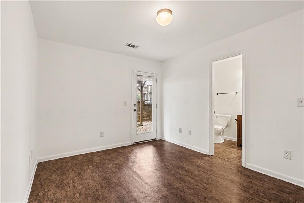 Empty room with dark wood-look flooring, a glass-paneled exterior door, and an adjoining bathroom.