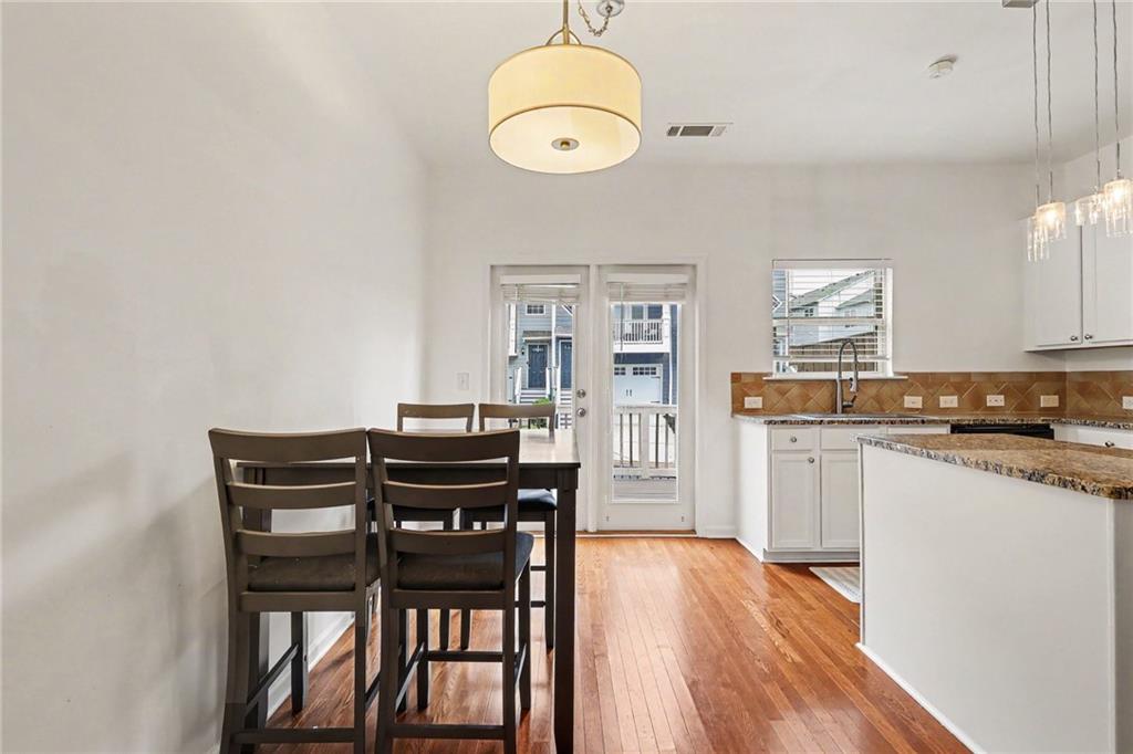 Kitchen and dining area with hardwood floors, dark table and chairs, and a glass door to the balcony.