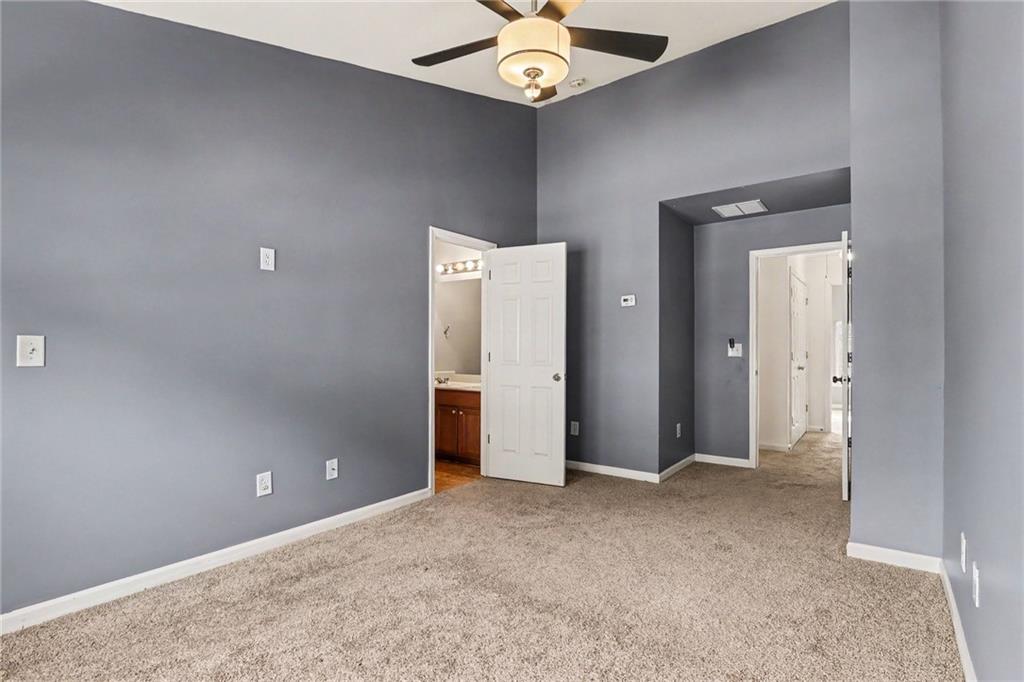 Empty carpeted bedroom with gray walls, ceiling fan, and open doors to a bathroom and hallway.