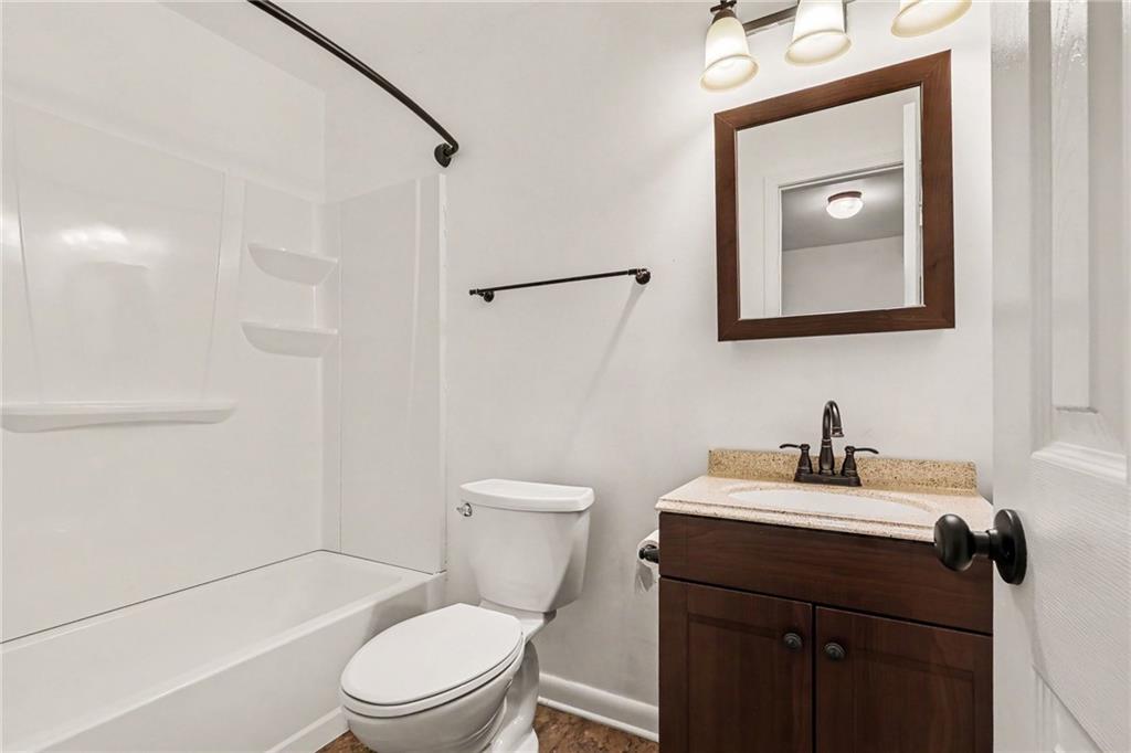 Bathroom with a white tub and shower, toilet, and dark wood vanity with framed mirror.