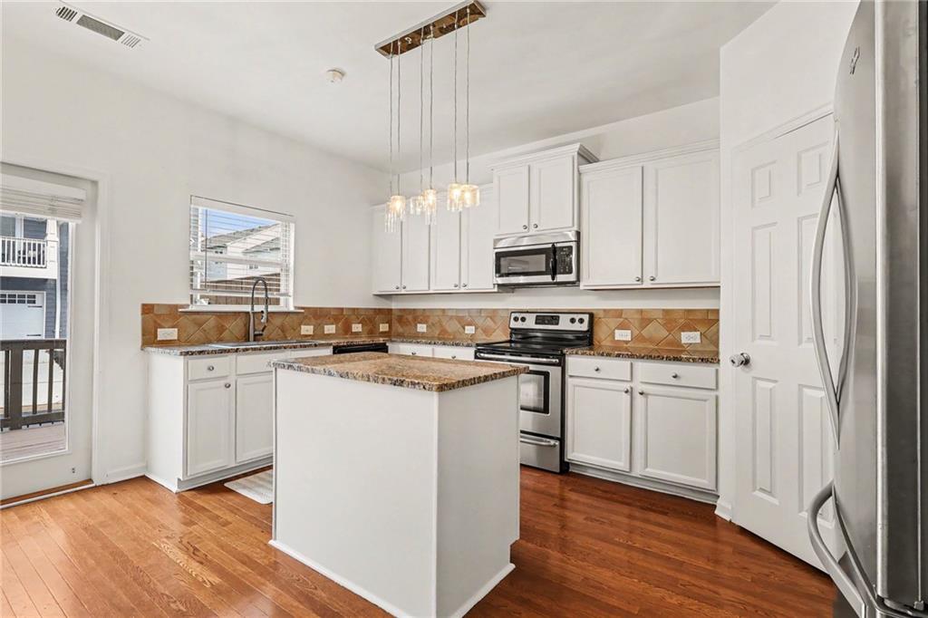 Kitchen with a central island, white cabinets, stainless steel appliances, and hardwood floors.