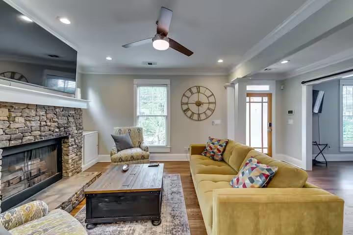 Living room with a stone fireplace, yellow sectional sofa, and large wall clock.