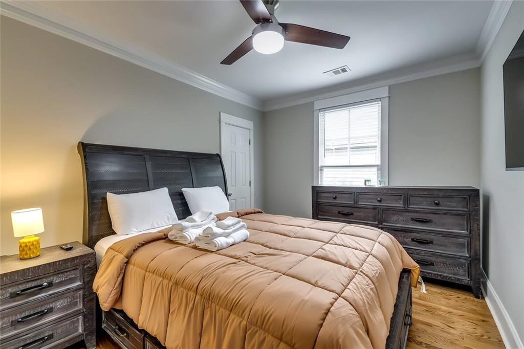 Staged bedroom with a tan quilt, dark wood furniture, and a ceiling fan.