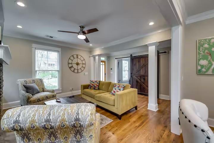 Furnished bedroom with a patterned bed, yellow sofa, and dark barn-style door.