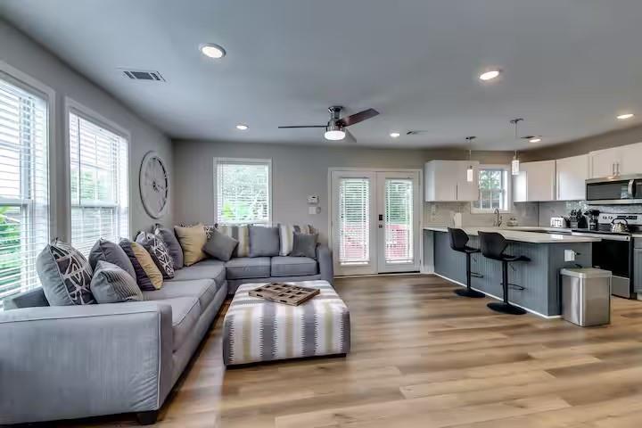 Open-plan living room and kitchen with a gray sectional, wood floors, and a dark island.