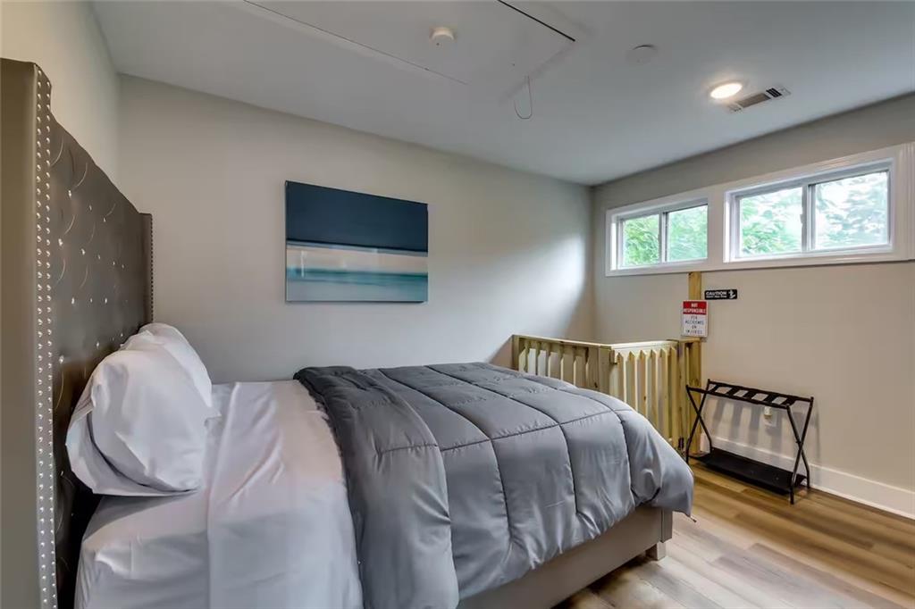 Bedroom with a gray-covered bed, blue abstract wall art, high windows, and a wooden safety gate.