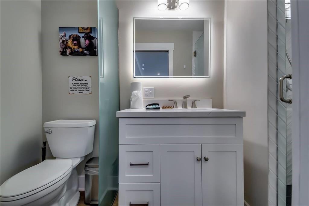 Bathroom with a white vanity, illuminated mirror, toilet, and glass shower partition.
