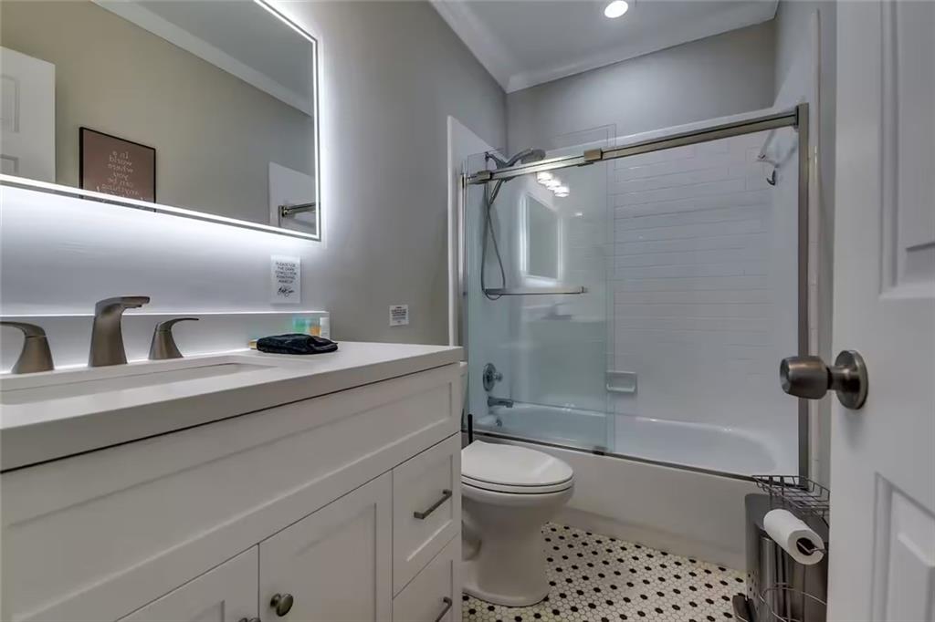 Bathroom with an illuminated mirror, white vanity, and tub-shower behind sliding glass doors.
