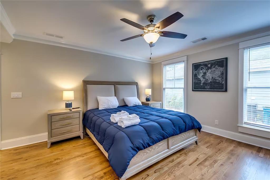 Bedroom with a navy blue bed, hardwood floors, two windows, and a ceiling fan.