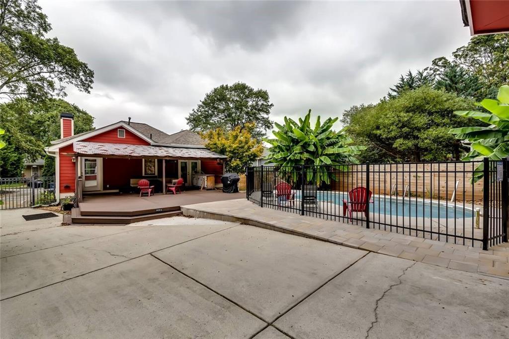 Backyard pool beside a covered patio with red chairs and a spacious concrete patio.
