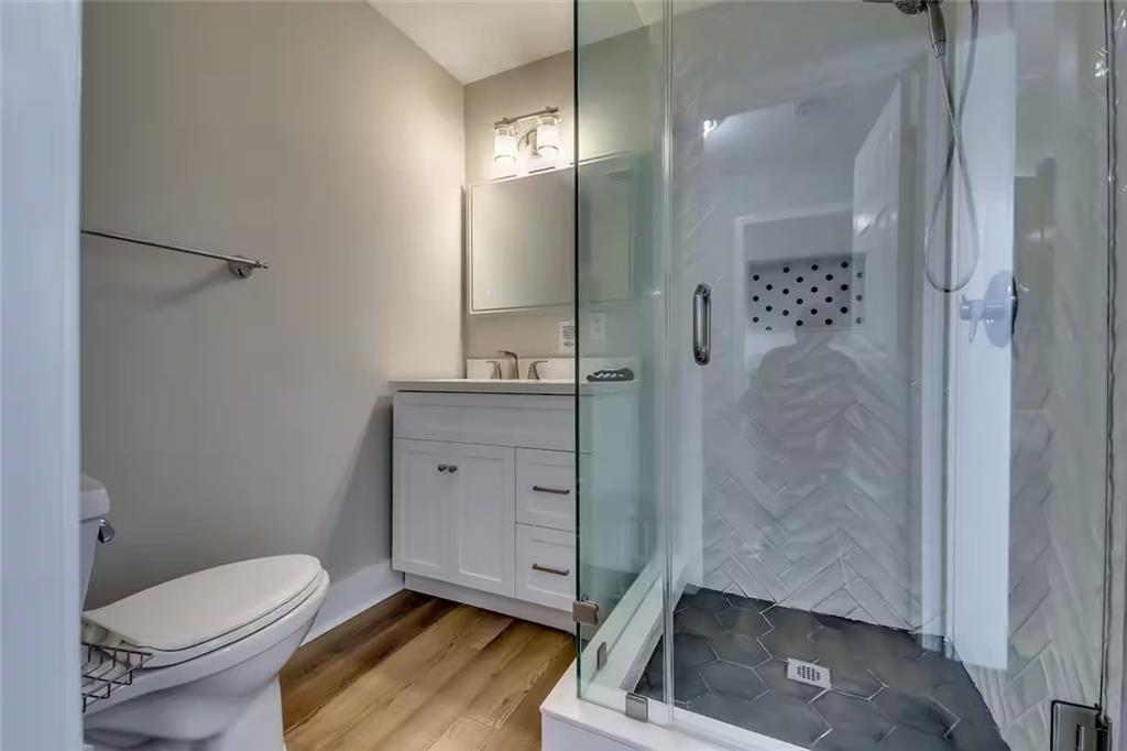 Bathroom with a glass shower, white herringbone tile, dark hexagonal shower floor, and warm wood flooring.
