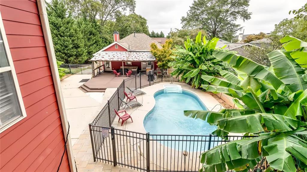 Backyard swimming pool with black fencing, red lounge chairs, and a covered pavilion.
