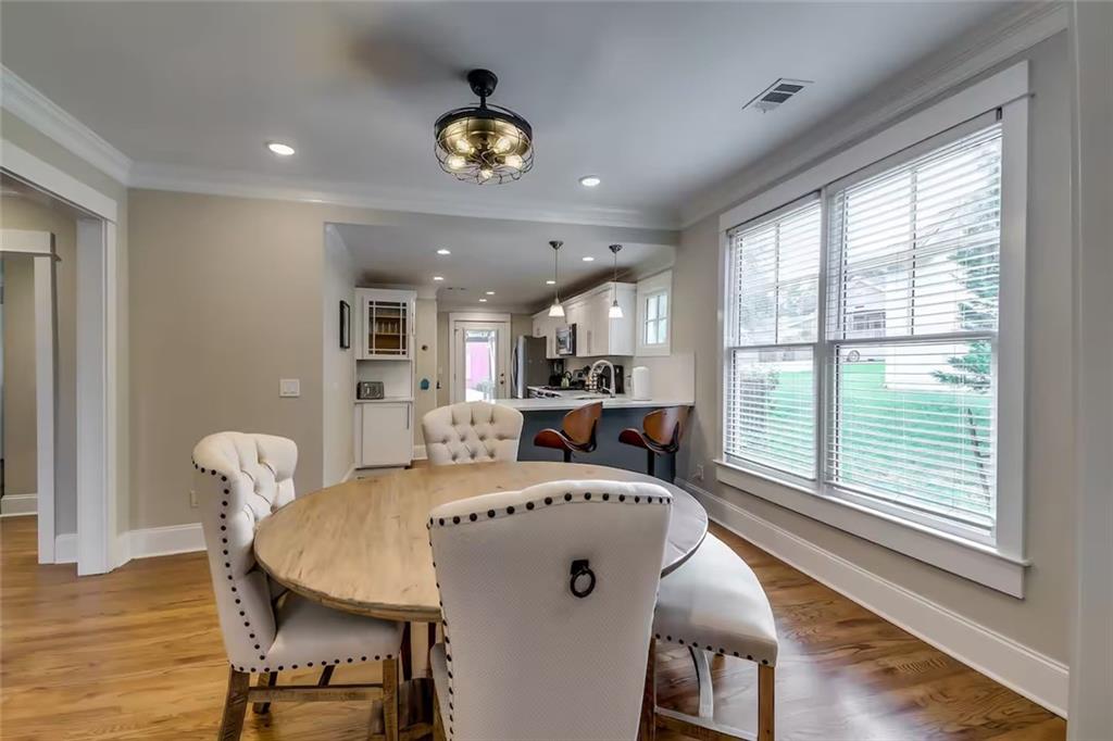 Dining area with a round wood table, white upholstered chairs, and open kitchen beyond.