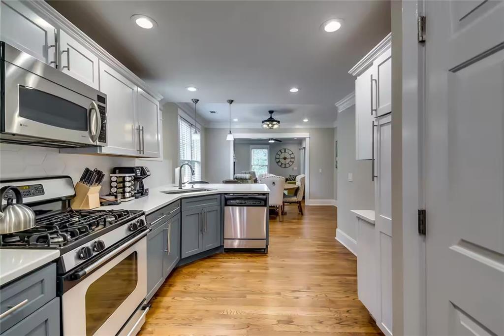 Kitchen with gray lower cabinets, stainless steel appliances, and wood floors leading to a sitting area.