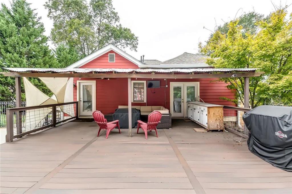 Covered backyard deck with red Adirondack chairs, an outdoor sofa, and a grill.