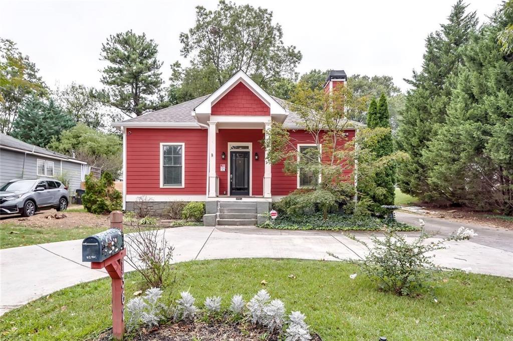 Red house with white trim and a covered front porch, framed by mature trees and a foreground mailbox.