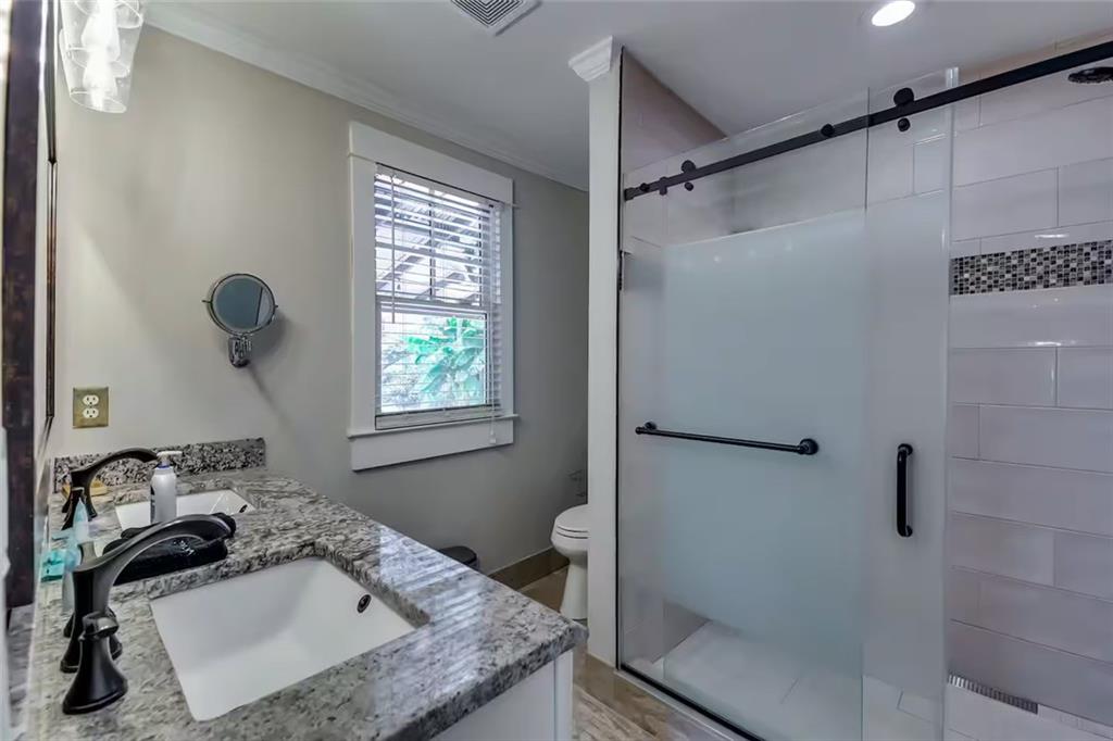 Bathroom with a granite vanity, frosted-glass shower, black grab bars, and a window with white blinds.