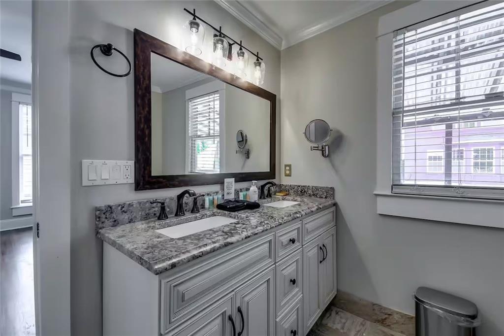 Bathroom vanity with two sinks, a speckled stone countertop and a large window with blinds.
