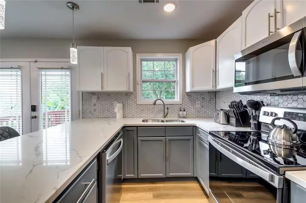 Kitchen with white quartz counters, gray cabinets, hexagonal backsplash, and stainless steel appliances.